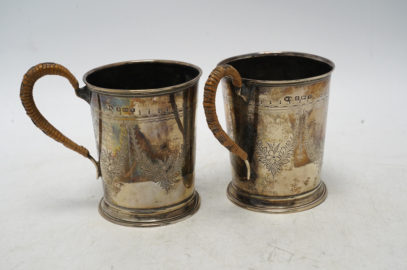 A pair of George V engraved silver mugs, with rattan handles, William Aitken, Birmingham, 1920, height 95mm, gross weight 5.9oz. Condition - fair